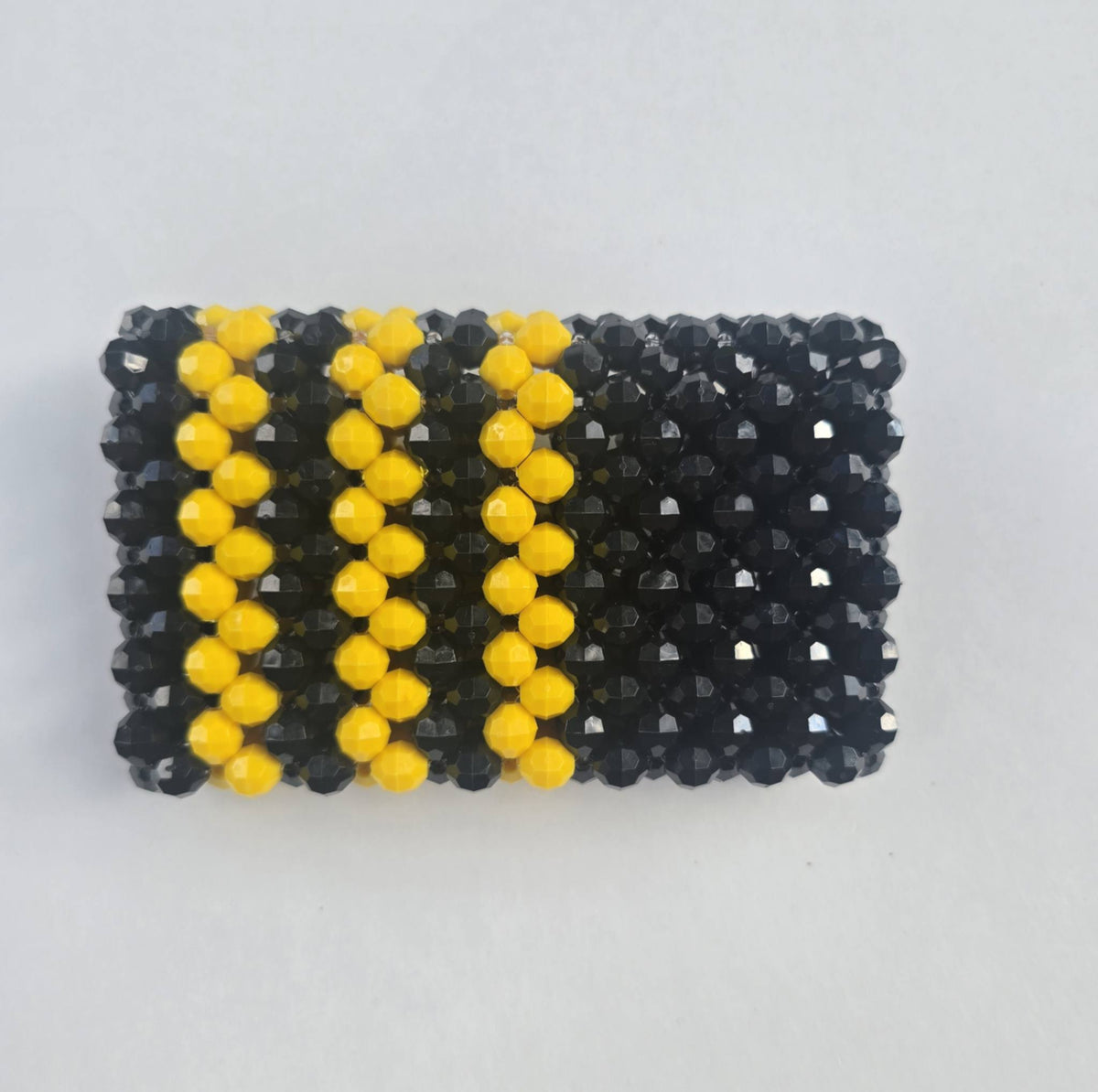 A beaded handmade wallet, featuring a black base with three vertical stripes of yellow beads, photographed on a light gray background.