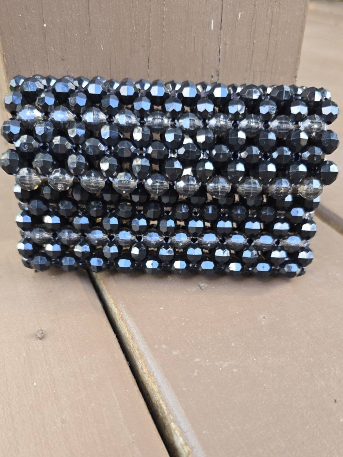 A rectangular wallet made of 8mm acrylic faceted black beads, resting on a brown wooden surface.