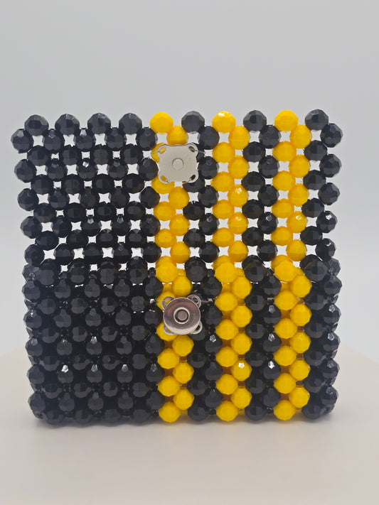 A square beaded wallet featuring a black and yellow striped pattern, secured with a silver-tone magnetic snap closure, set against a plain light background.