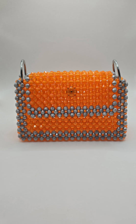 A small rectangular handbag covered in bright orange beads with a silver-gray beaded border and silver metal side rings, shown against a plain light gray background.