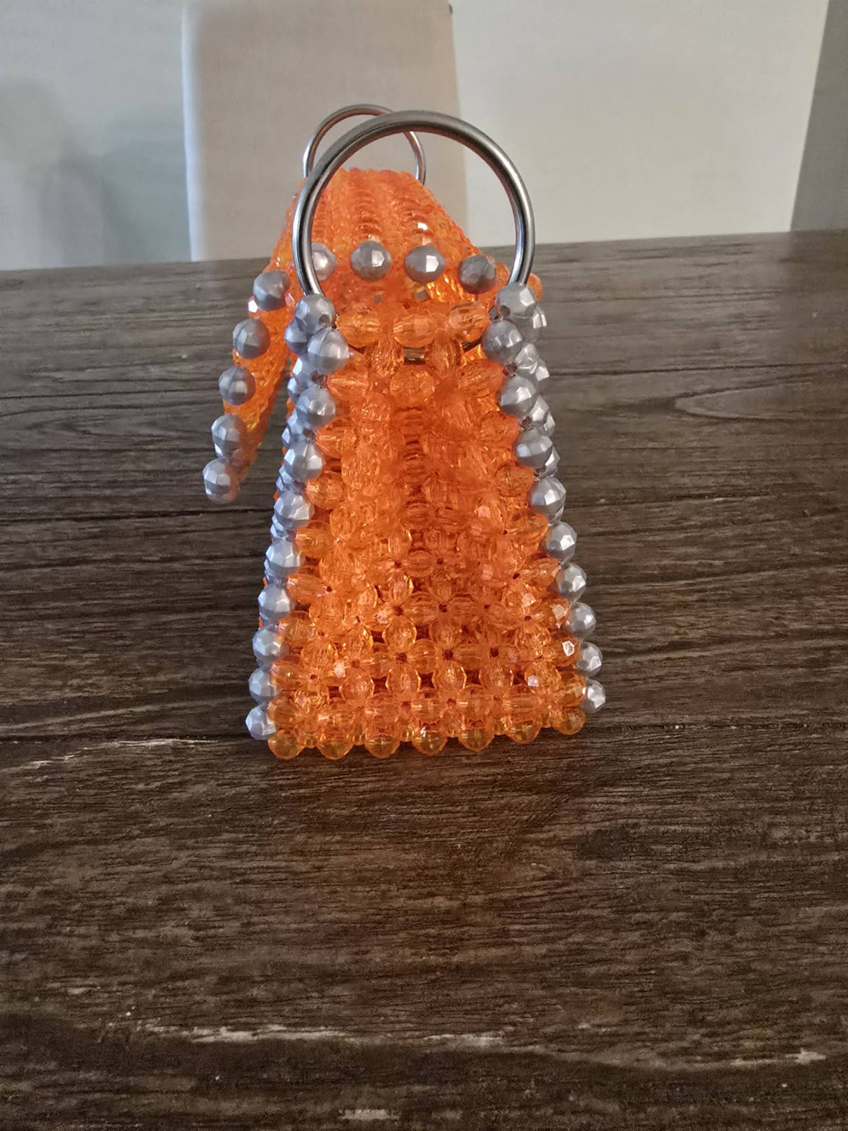 An orange beaded handbag with silver bead accents and a silver metal key ring, displayed on a dark wooden tabletop.