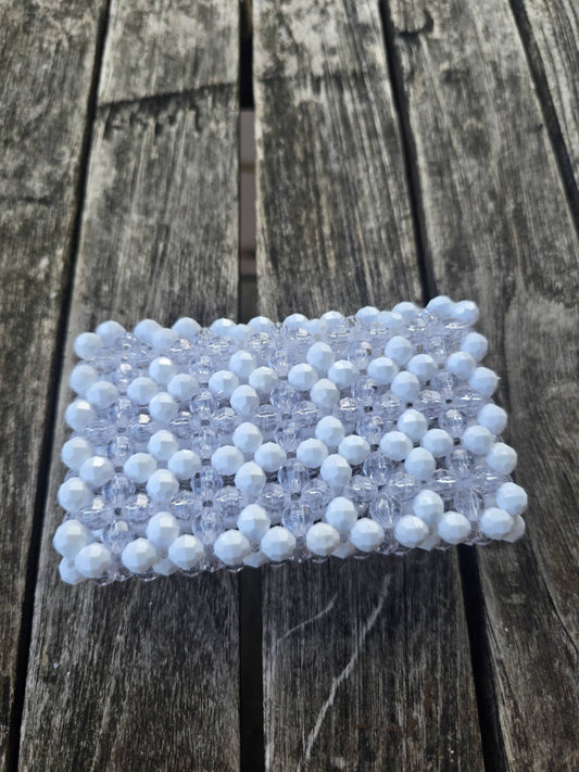 A handmade wallet, covered in white faceted beads with a clear beaded border, placed on a weathered gray wooden plank surface.